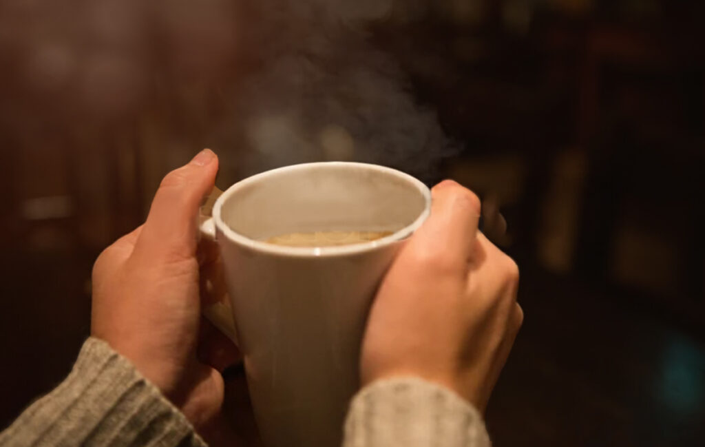 Close-up of hands holding a steaming cup of coffee, symbolizing Ricco Coffee’s promise of freshness, quality roasting, and airtight packaging technology